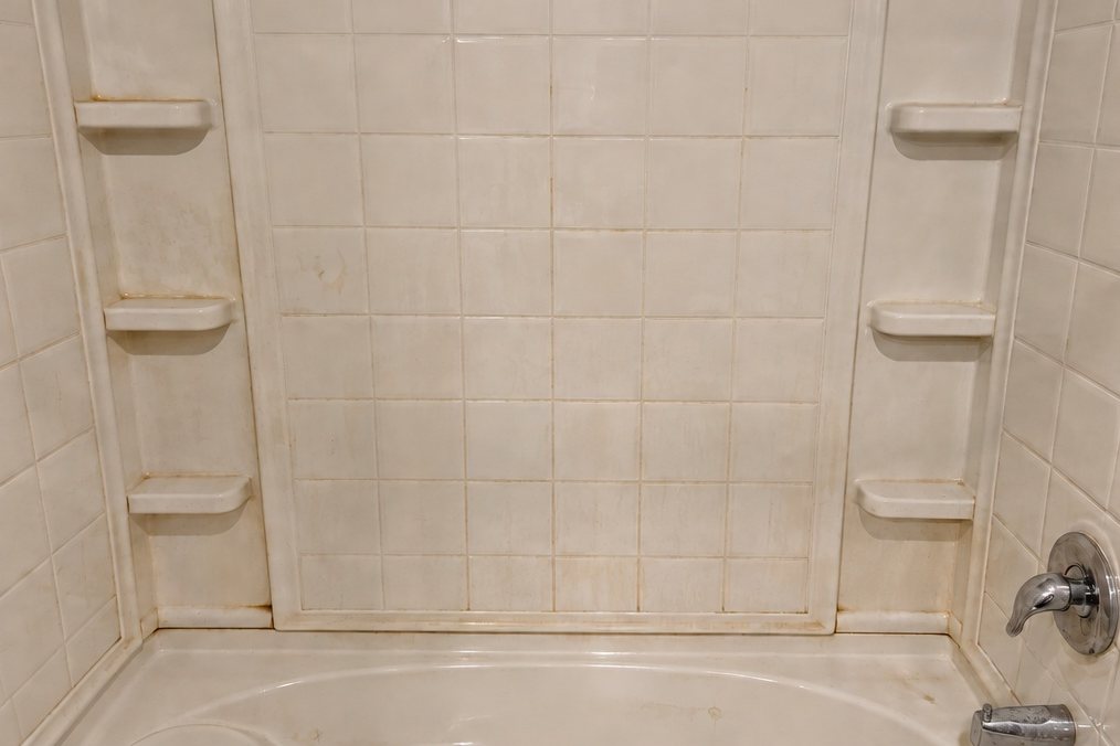 Tub and shower surround in North Las Vegas before Pure Space cleaning, with orange hard-water staining in the grout lines and on the shelves