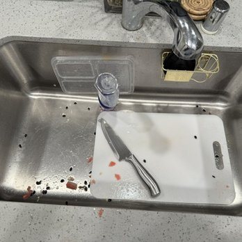Kitchen sink before Pure Space cleaning, with food scraps, a cutting board and a knife left in the basin